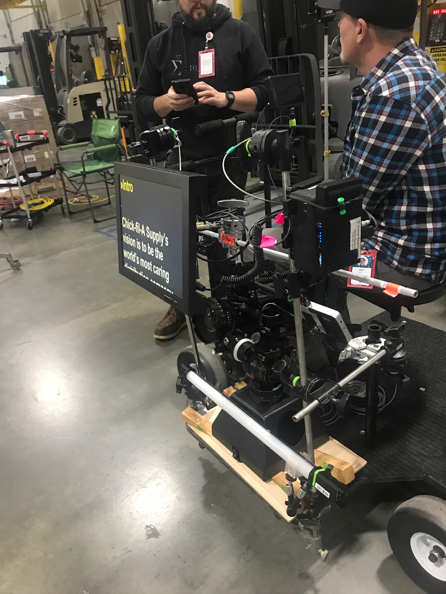 Cart-mounted cinema camera and teleprompter rig with operators in a warehouse