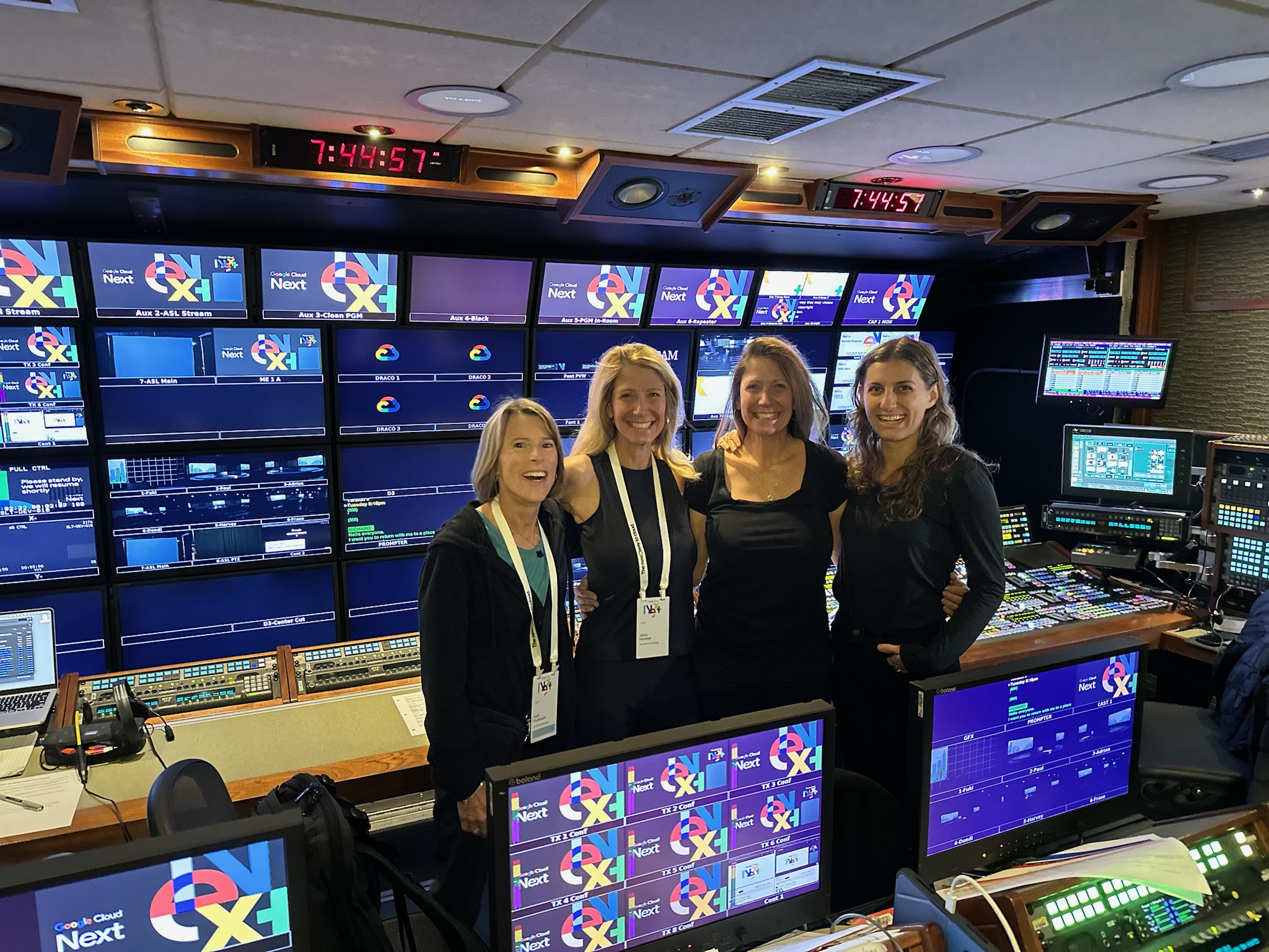 Four B Prompt operators in a broadcast control room in front of a wall of program monitors