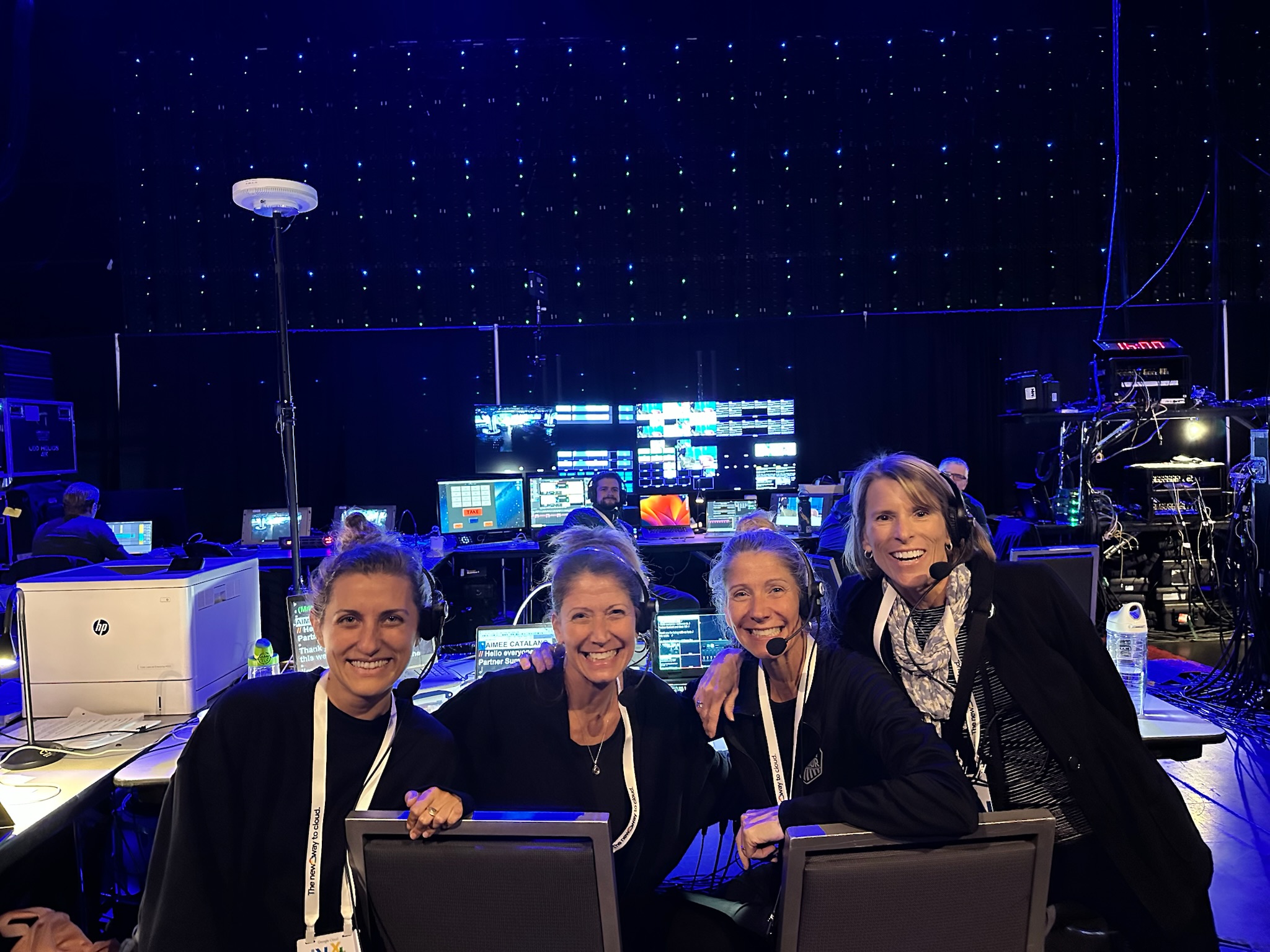 Four B Prompt operators in headsets smiling at a production control station with a starlit blue backdrop